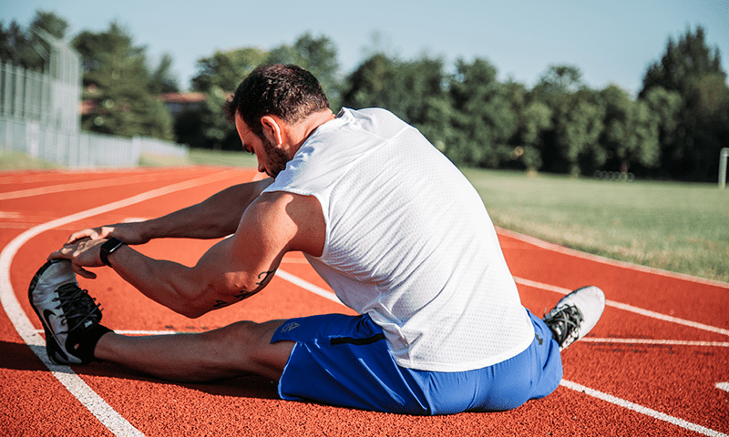 A photo of a man sitting down on an athletics track stretching his legs